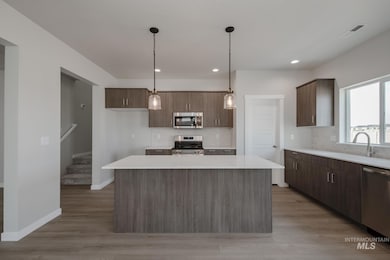 Kitchen featuring pendant lighting, appliances with stainless steel finishes, a kitchen island, light wood-type flooring, and modern cabinets