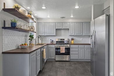 Kitchen featuring gray cabinetry, appliances with stainless steel finishes, open shelves, butcher block counters, and decorative backsplash