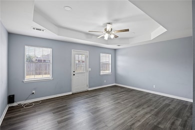 Spare room featuring a tray ceiling, dark wood-style floors, and ceiling fan