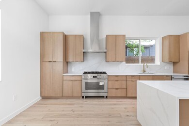 Kitchen with stainless steel range with gas stovetop, wall chimney exhaust hood, light wood finished floors, and modern cabinets