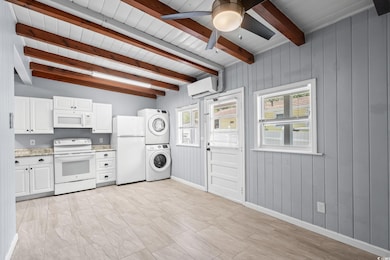 Kitchen with white appliances, white cabinetry, stacked washing machine and dryer, an AC wall unit, and wood walls