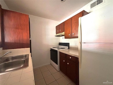 Kitchen with tile countertops, white appliances, visible vents, under cabinet range hood, and a sink