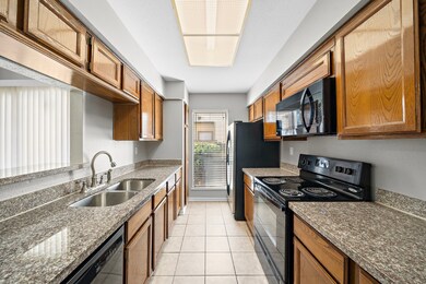 Modern kitchen with granite countertops, wooden cabinets, and tile flooring. Equipped with black appliances and a large window for natural light.