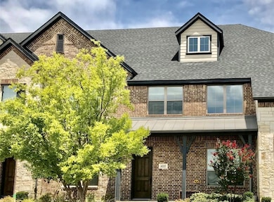 View of front of home with brick siding, a shingled roof, a standing seam roof, and covered porch