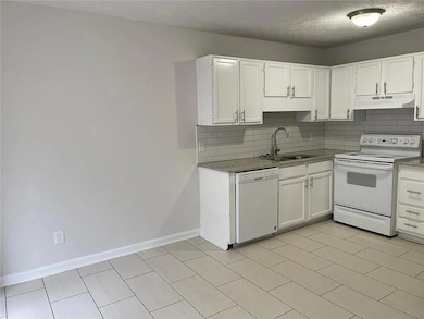 Kitchen with white appliances, under cabinet range hood, a sink, tasteful backsplash, and a textured ceiling
