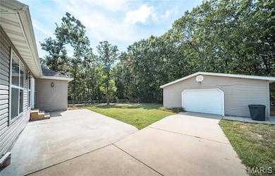 View of yard featuring an outbuilding, a patio, concrete driveway, a detached garage, and view of wooded area