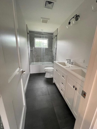 Bathroom featuring combined bath / shower with glass door and double vanity