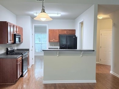 Kitchen featuring black appliances, light wood-style flooring, a breakfast bar, dark countertops, and hanging light fixtures