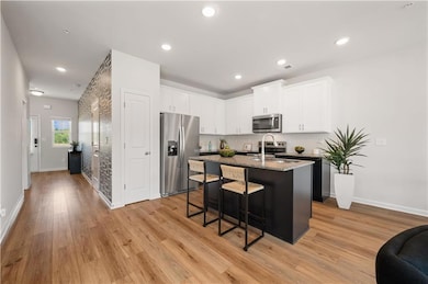 Kitchen featuring white cabinets, an island with sink, appliances with stainless steel finishes, light stone counters, and a kitchen breakfast bar