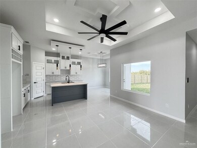 Kitchen featuring white cabinetry, a center island with sink, a tray ceiling, decorative light fixtures, and backsplash