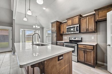 Kitchen with appliances with stainless steel finishes, lofted ceiling, an island with sink, decorative backsplash, and light stone countertops