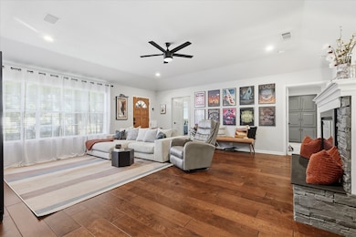Living area featuring dark wood-type flooring, a stone fireplace, recessed lighting, and ceiling fan