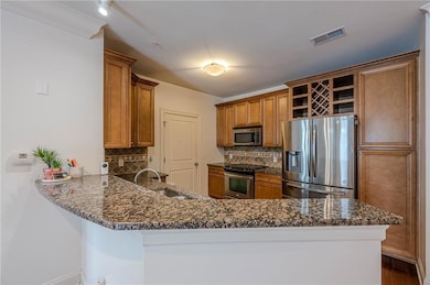 Kitchen with stainless steel appliances, a sink, open shelves, brown cabinets, and a peninsula