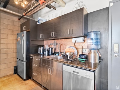 Kitchen featuring appliances with stainless steel finishes, dark stone counters, dark brown cabinets, and concrete flooring