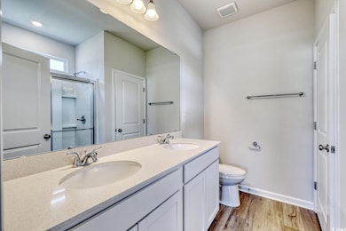 Full bath featuring wood finished floors, a shower stall, toilet, baseboards, and double vanity