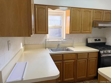 Kitchen featuring light countertops, tasteful backsplash, brown cabinetry, stainless steel gas range, and under cabinet range hood