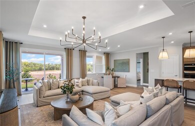 Model RepresentationLiving area with a tray ceiling, a chandelier, crown molding, recessed lighting, and baseboards.