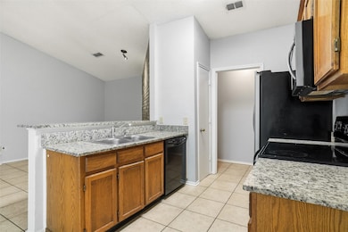 Kitchen featuring brown cabinets, a peninsula, light tile patterned flooring, and black dishwasher