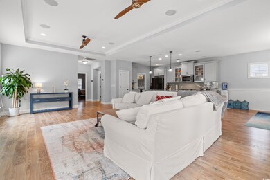 Living room with ceiling fan, light wood finished floors, a raised ceiling, and recessed lighting