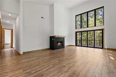 Unfurnished living room with a towering ceiling, a glass covered fireplace, light wood-type flooring, and recessed lighting