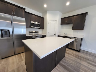 Kitchen featuring appliances with stainless steel finishes, dark brown cabinets, recessed lighting, light wood-type flooring, and a kitchen island