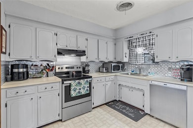 Kitchen with appliances with stainless steel finishes, white cabinets, and sink