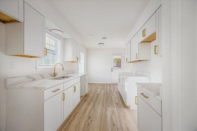 Kitchen featuring white cabinets, light wood-style flooring, and light stone counters