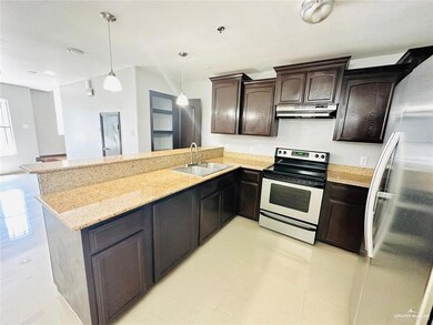Kitchen with dark brown cabinets, hanging light fixtures, a sink, a peninsula, and appliances with stainless steel finishes