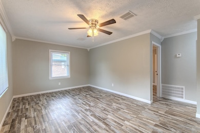 Empty room featuring wood finished floors, a ceiling fan, a textured ceiling, and ornamental molding