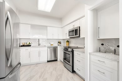 Crisp white kitchen with recent cabinetry, stone counters and stainless appliances.