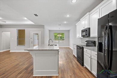 Kitchen with black appliances, recessed lighting, light stone counters, dark wood-style flooring, and an island with sink