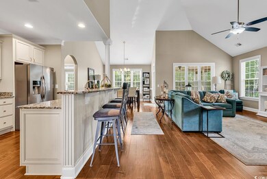 Kitchen with a ceiling fan, high vaulted ceiling, wood finished floors, open floor plan, and light stone counters