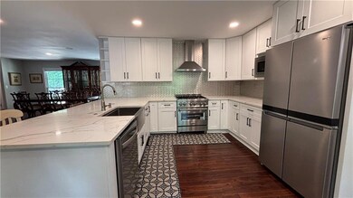 Kitchen featuring appliances with stainless steel finishes, wall chimney range hood, a sink, a peninsula, and light stone countertops