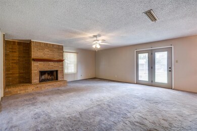 Unfurnished living room with ceiling fan, a textured ceiling, light colored carpet, and a brick fireplace