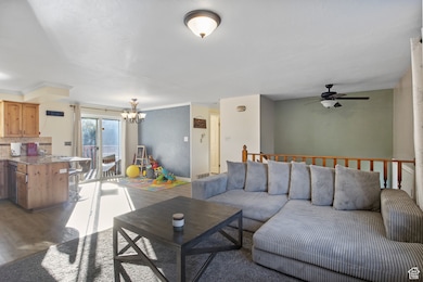 Living room with a chandelier, dark wood-style floors, ornamental molding, and ceiling fan