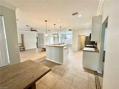 Kitchen featuring pendant lighting, a kitchen island with sink, ceiling fan with notable chandelier, crown molding, and light tile patterned flooring