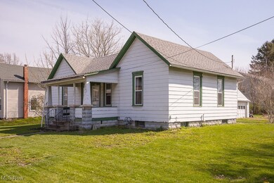 View of front of home featuring a front yard, a shingled roof, covered porch, and a garage