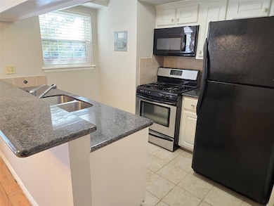 Kitchen with black appliances, tasteful backsplash, a peninsula, a breakfast bar area, and dark stone counters