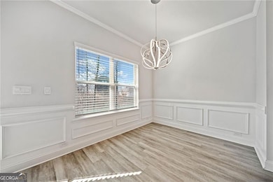 Unfurnished dining area featuring light wood-type flooring, a wainscoted wall, crown molding, and an inviting chandelier