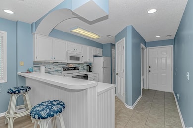 Kitchen with white cabinets, backsplash, a peninsula, light countertops, and a textured ceiling
