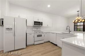 Kitchen with white appliances, light countertops, decorative light fixtures, white cabinets, and light wood-style flooring