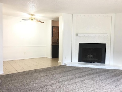 Unfurnished living room with tile patterned flooring, ceiling fan, carpet, a textured ceiling, and a fireplace