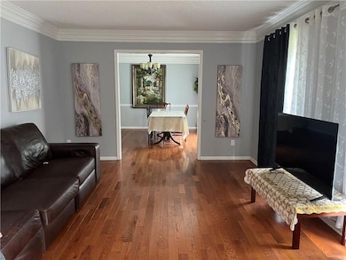 Living area with dark wood-type flooring, ornamental molding, and a chandelier
