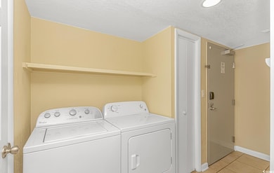 Washroom with a textured ceiling, light tile patterned floors, and washer and clothes dryer