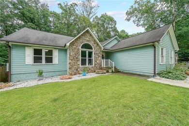 Ranch-style home with a front yard, a shingled roof, and stone siding