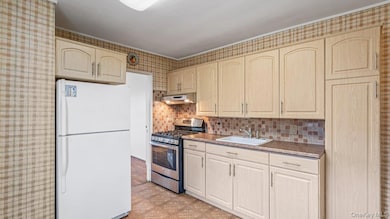 Kitchen featuring freestanding refrigerator, stainless steel range with gas cooktop, light floors, tasteful backsplash, and under cabinet range hood
