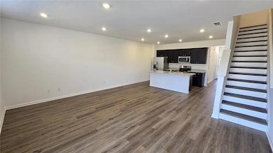 Unfurnished living room featuring stairs, dark wood-type flooring, baseboards, and recessed lighting