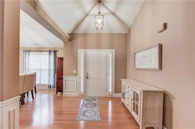 Foyer with light wood-style flooring, a wainscoted wall, a decorative wall, and high vaulted ceiling