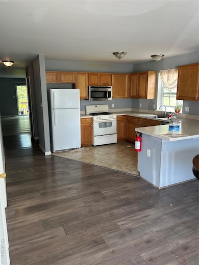 Kitchen with light countertops, stainless steel fridge, brown cabinets, white range with gas stovetop, and dark wood-style floors