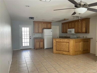 Kitchen featuring a peninsula, white appliances, a ceiling fan, brown cabinetry, and light tile patterned floors